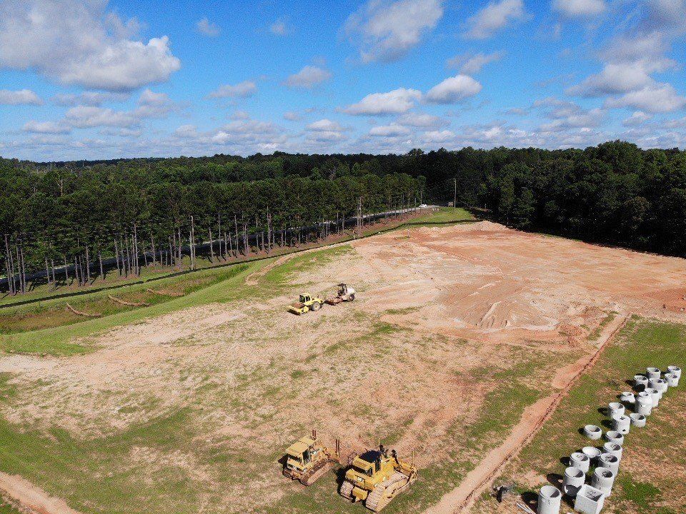 An aerial view of a construction site with a lot of dirt and trees in the background.