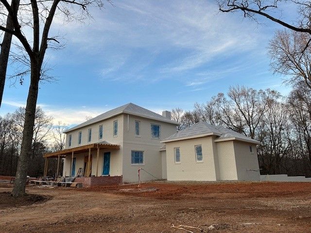 A two-story house under construction with an attached single-story structure, blue doors, and a cloudy sky.