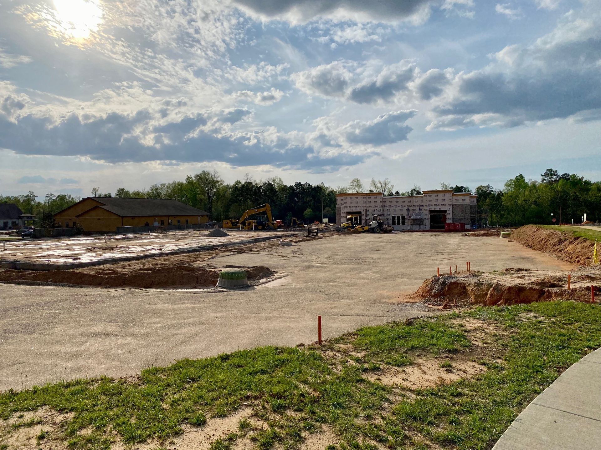A construction site with a building in the background and the sun shining through the clouds.