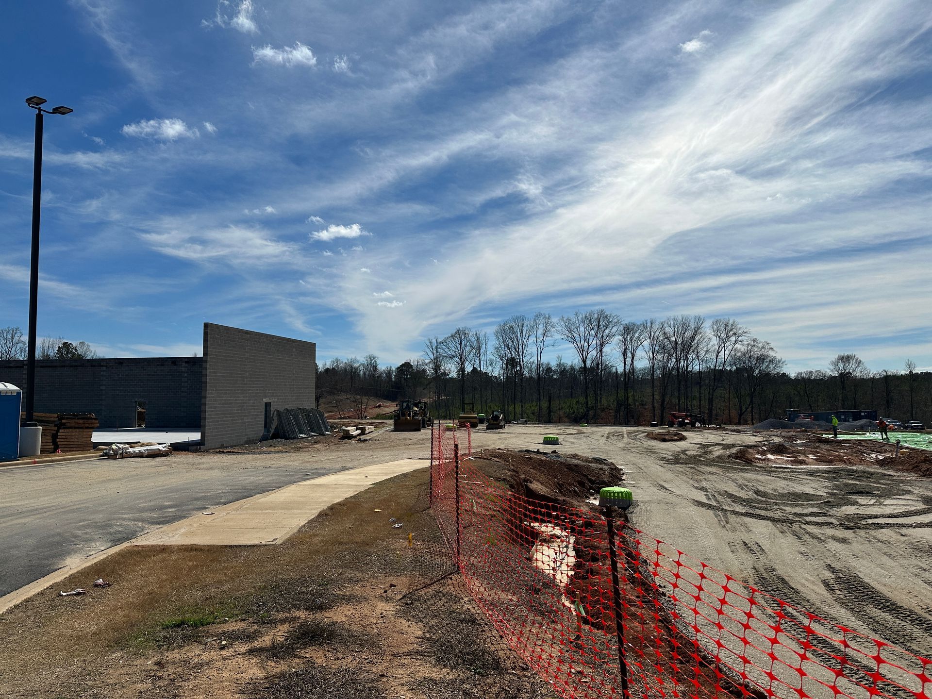 Construction site with orange safety fencing, dirt path, concrete walls, and a partly cloudy sky.