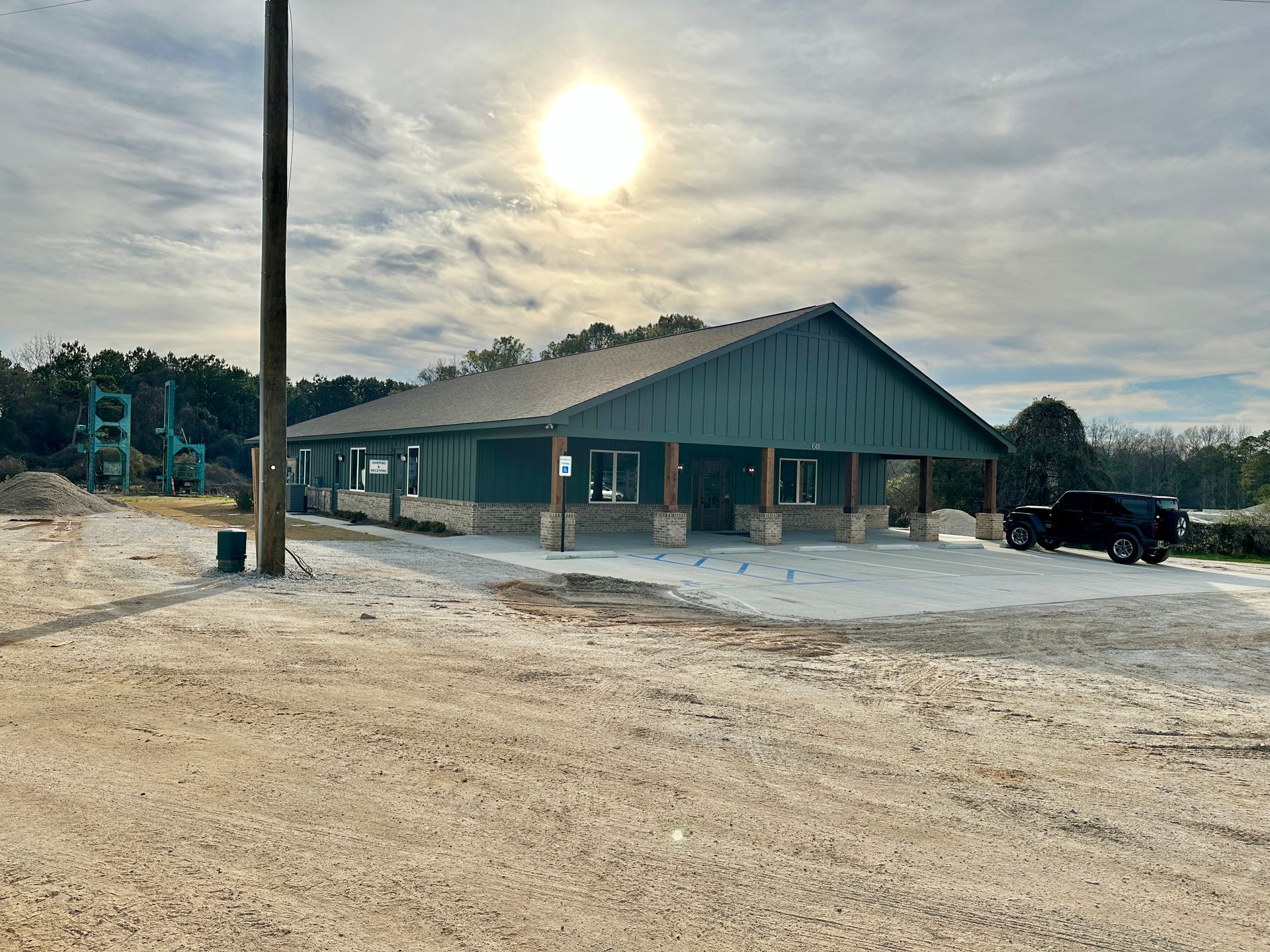 Green building with stone accents, parked truck, bright sun, gravel lot.