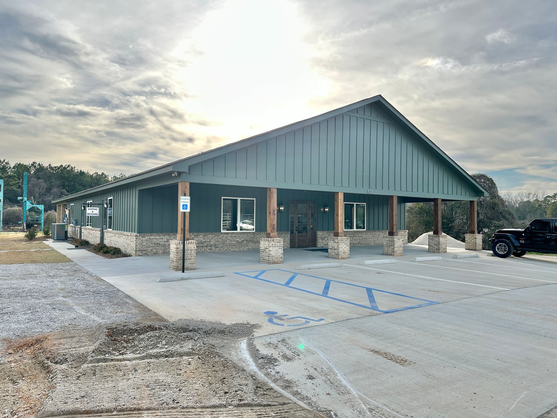 Green building with covered porch and accessible parking. Cloudy sky backdrop.