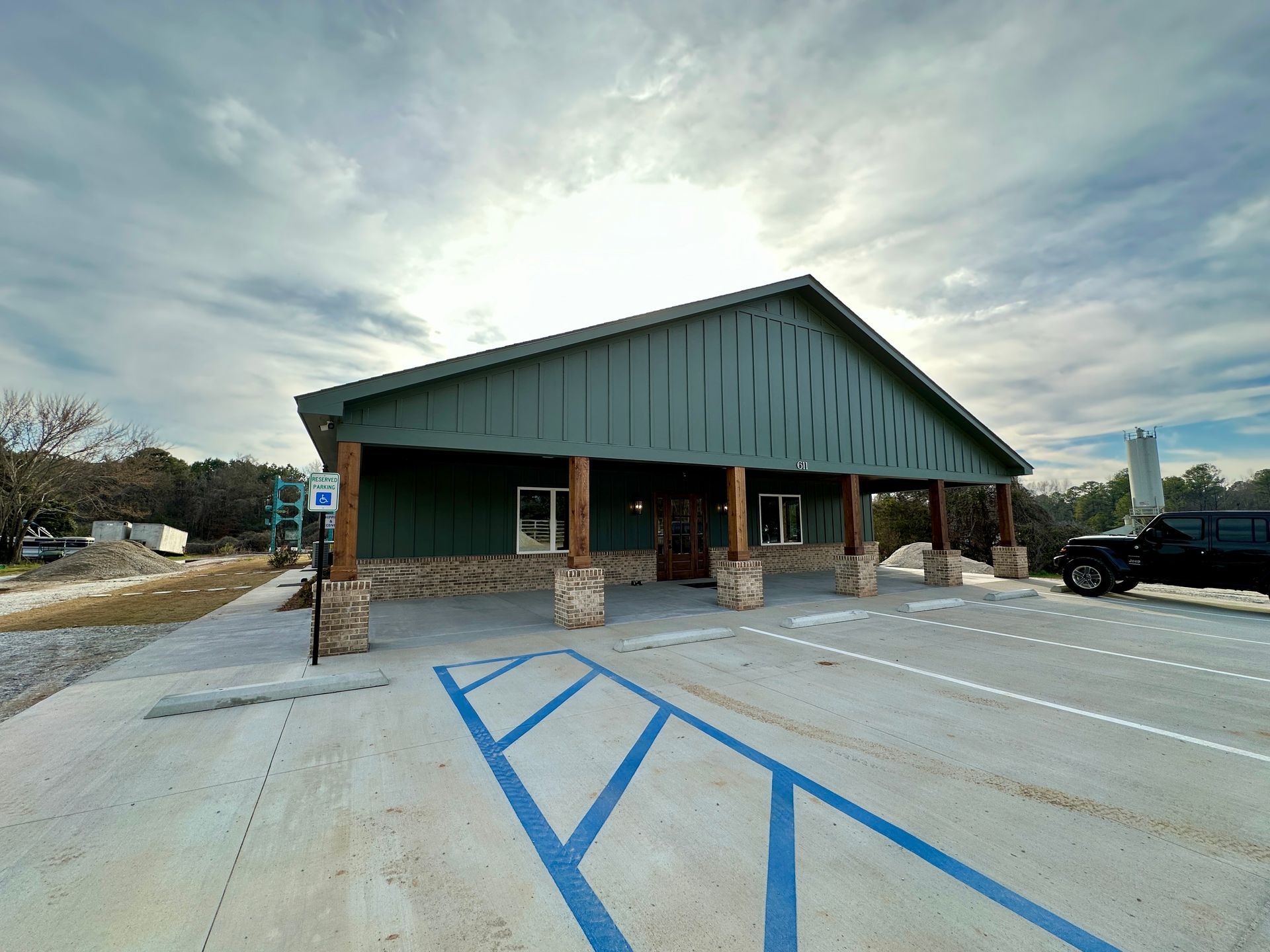 A teal-colored commercial building with accessible parking spots and a truck, under a cloudy sky.