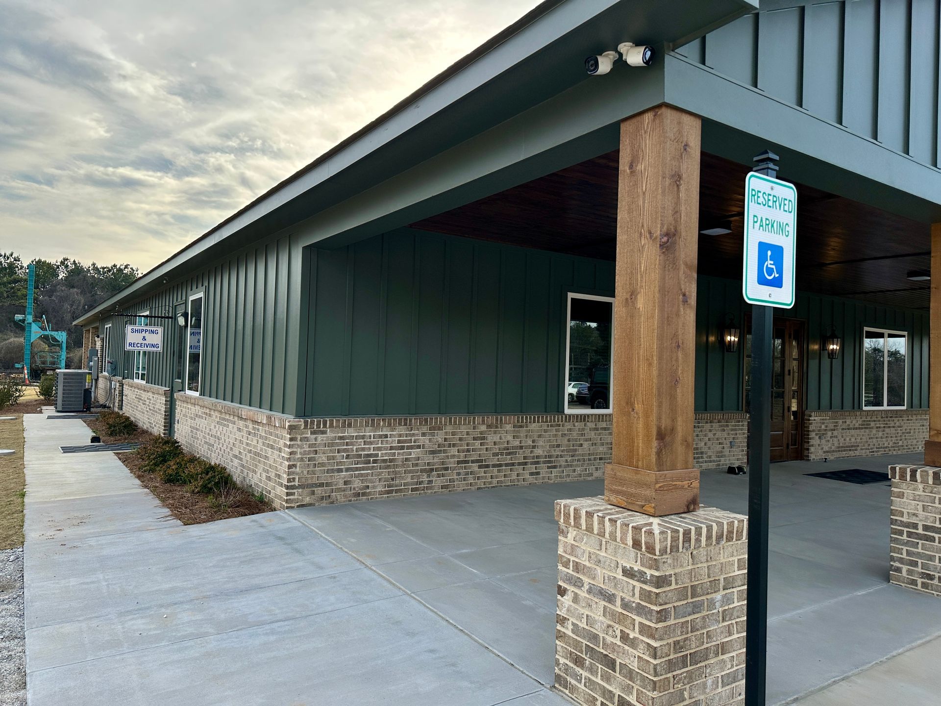 Exterior view of a green building with brick accents and a covered walkway. A handicap parking sign is visible.