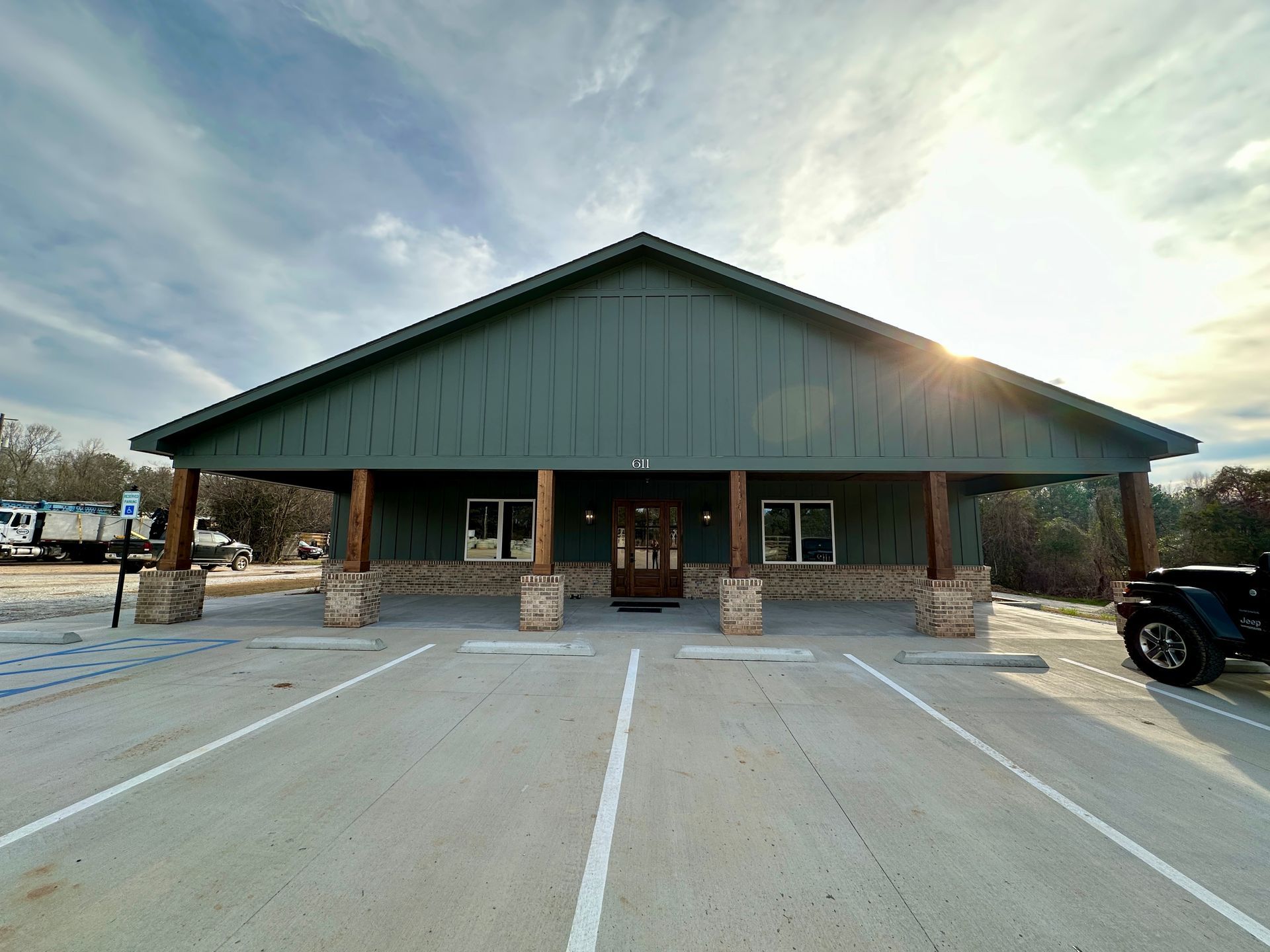 Green building with stone columns, covered porch, and parking in front under a cloudy sky.