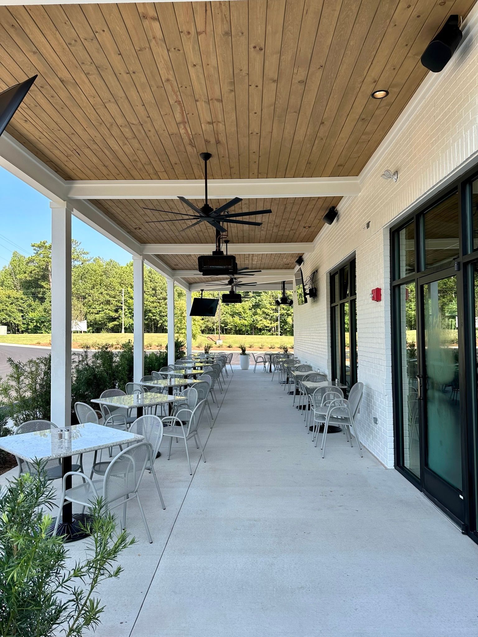 A long covered patio with tables and chairs and ceiling fans.