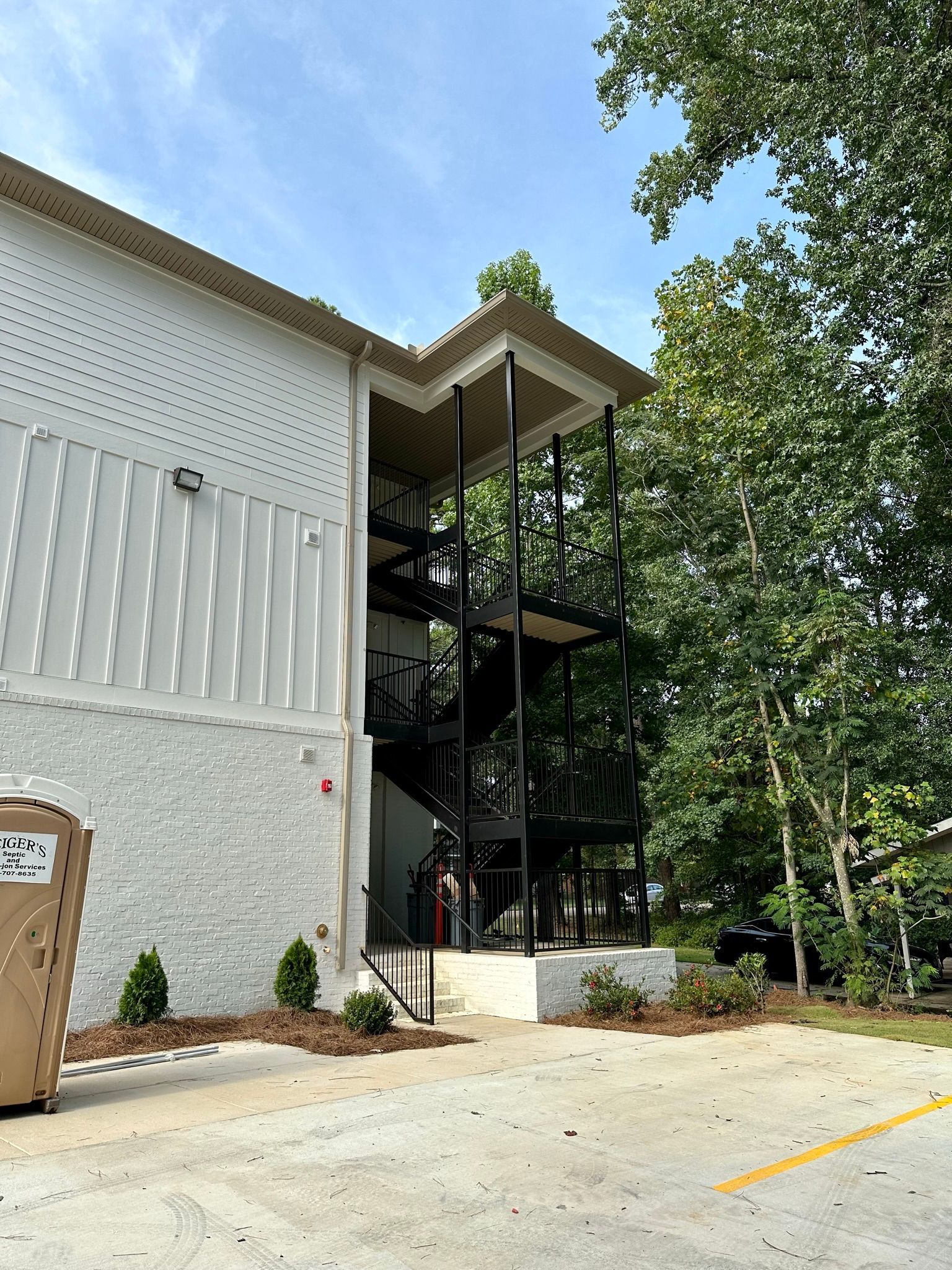 A large white building with stairs and a trash can in front of it.