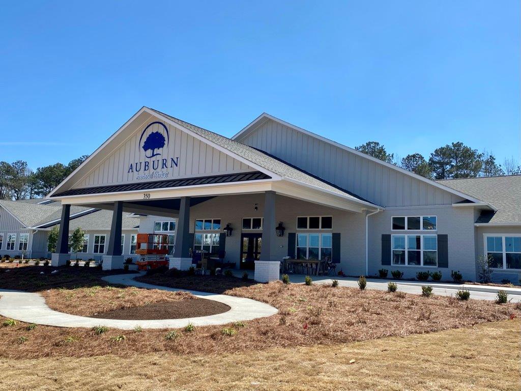 A large white business with a large porch and a tree on the front of it.