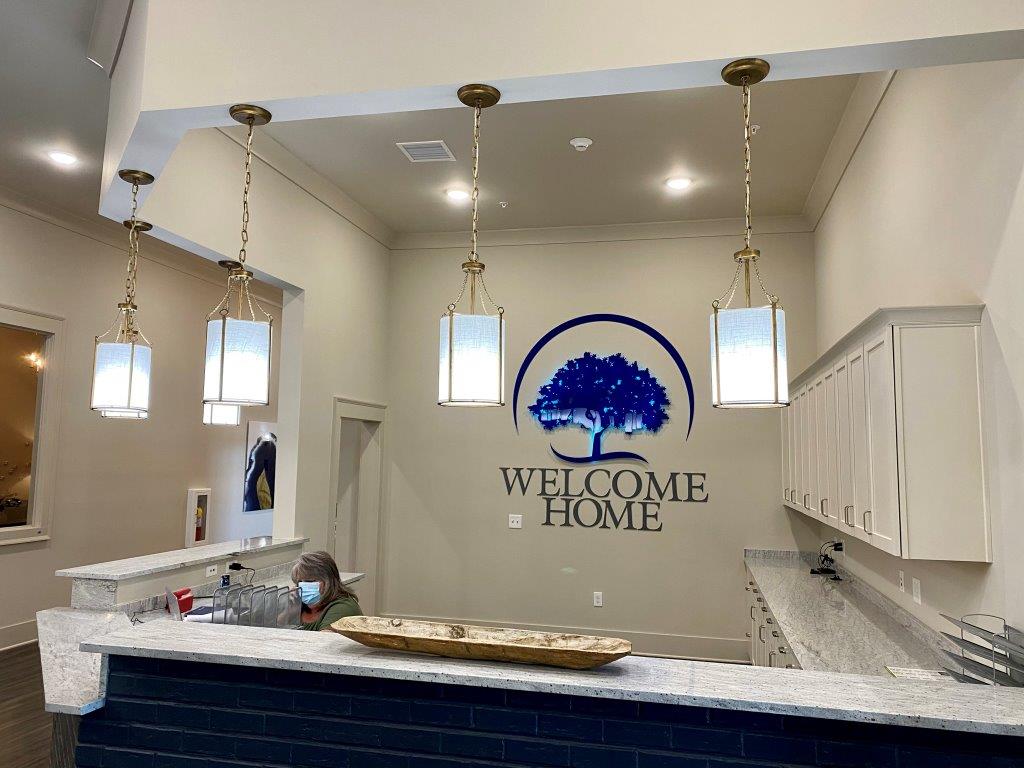 A woman is standing at a counter in a kitchen with a welcome home sign on the wall.