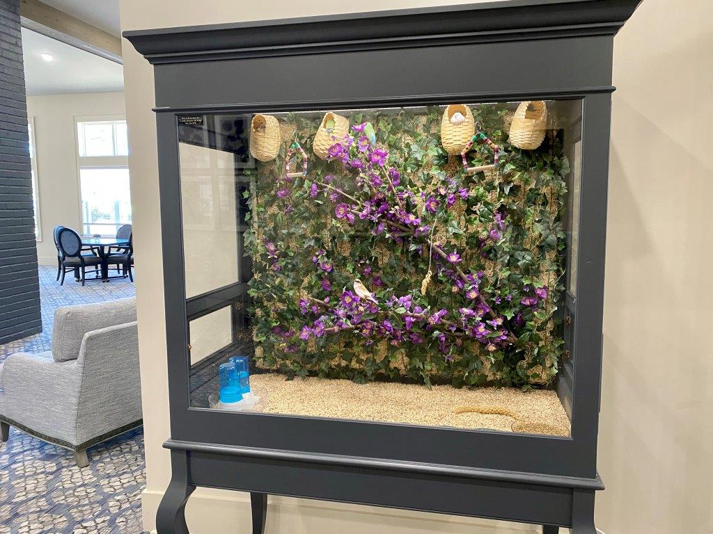 A large aquarium filled with purple flowers and birds in a living room.