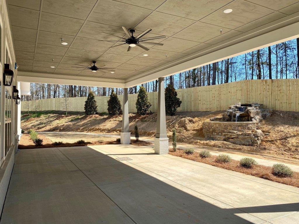 A large covered porch with a ceiling fan and trees in the background.
