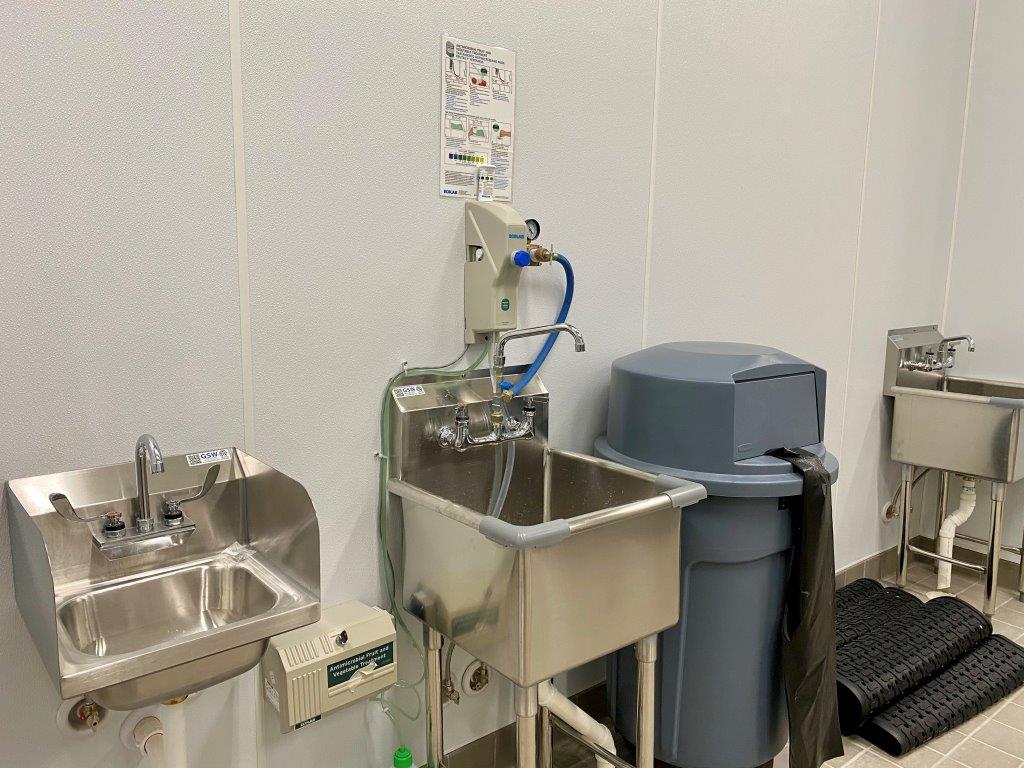 A kitchen with stainless steel sinks and trash cans.
