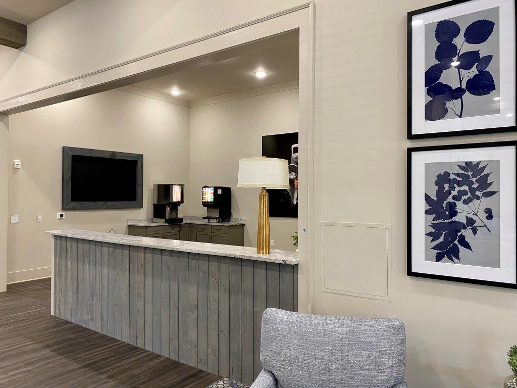 A living room with a desk , chair , lamp , television and paintings on the wall.