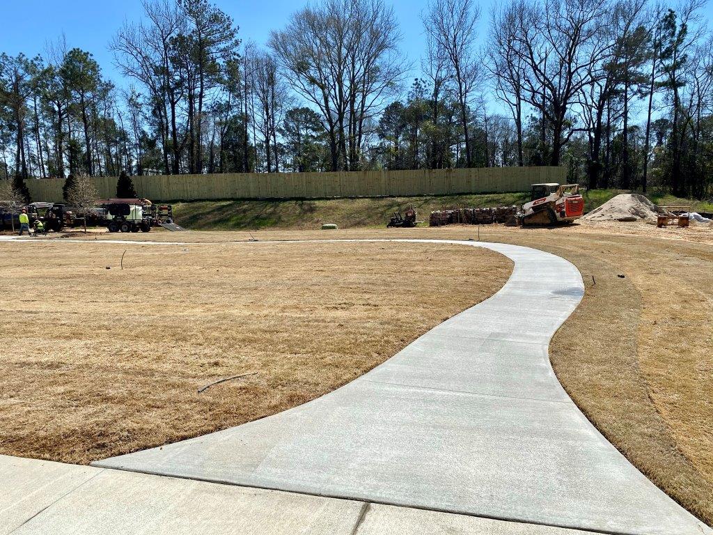 A concrete walkway going through a field with trees in the background.