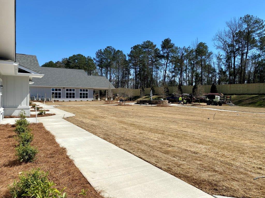 A concrete walkway leading to an assisted living facility with a large field in front of it.