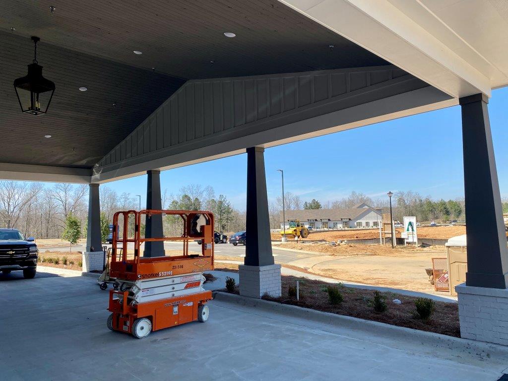 An orange scissor lift is parked under a canopy in a parking lot.