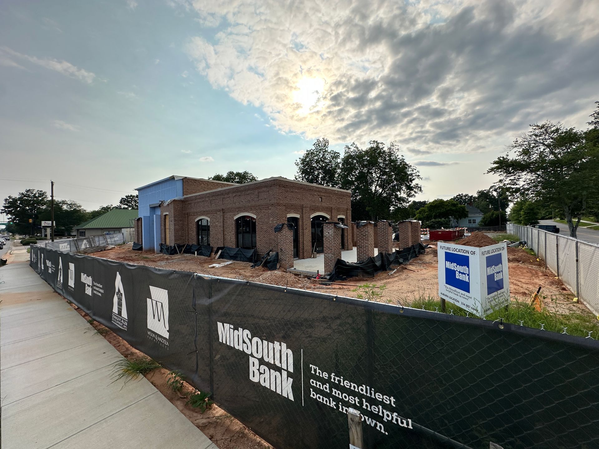 Partially built red brick bank under a blue sky, with black tarp and construction items in front.
