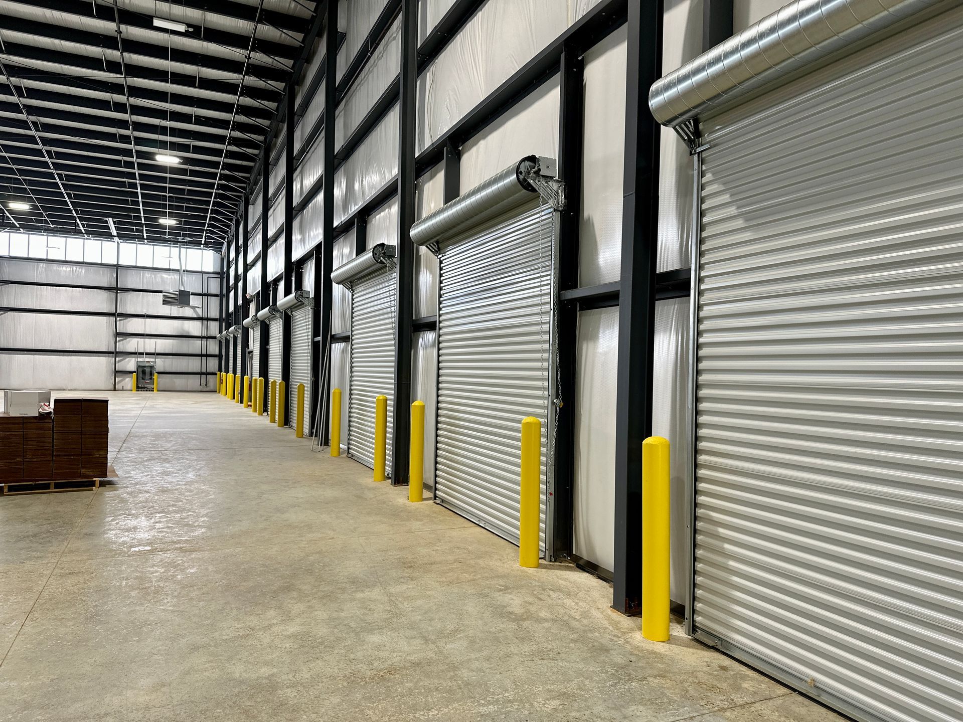 A large warehouse with a lot of roller doors and yellow poles.