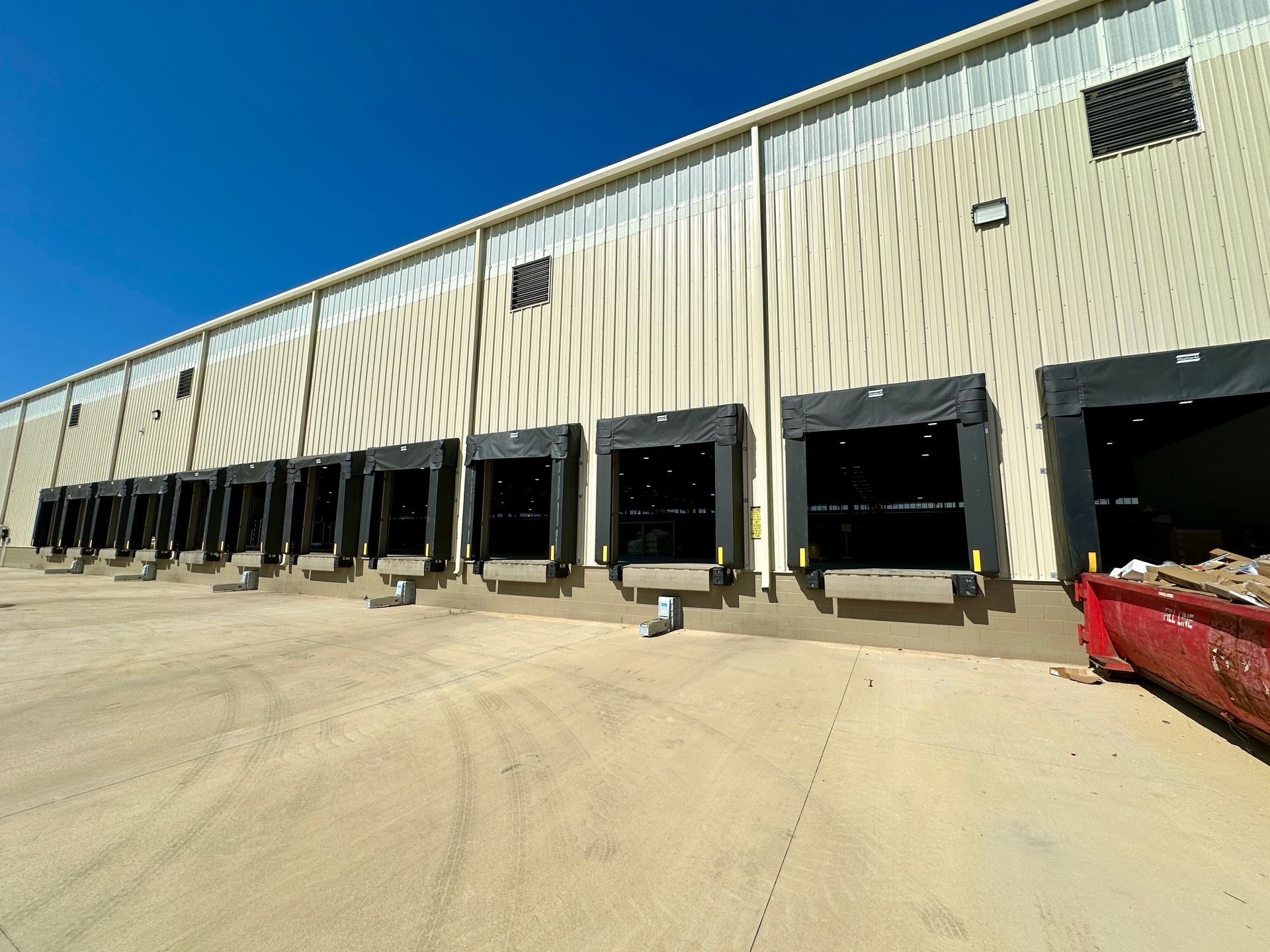 A large warehouse with lots of loading docks and a red dumpster in front of it.