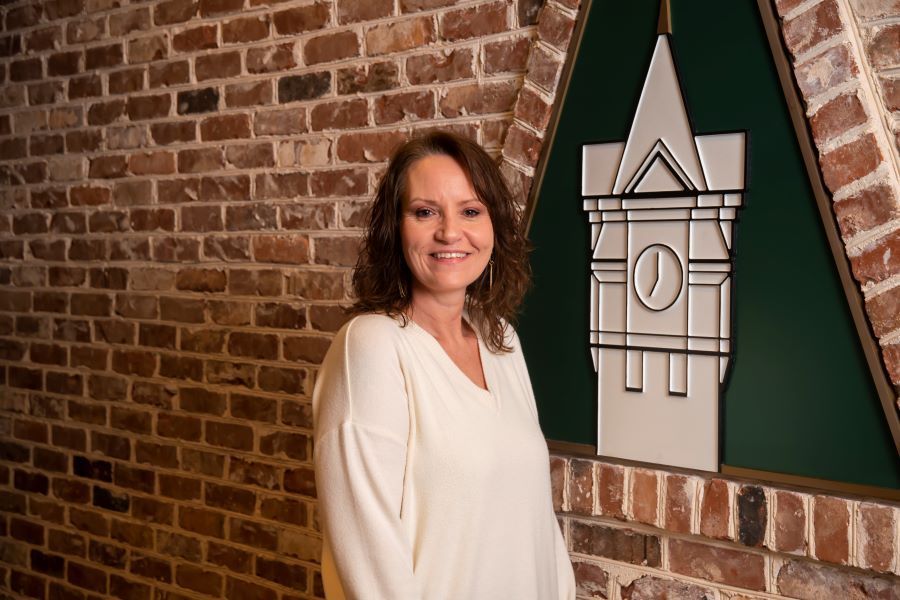Kelly Wester is standing in front of a brick wall with a clock tower on it.