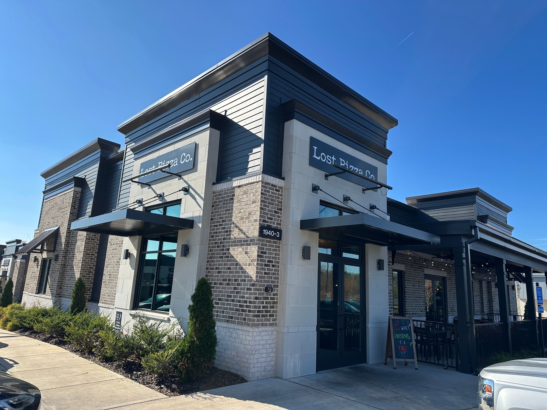 A modern restaurant building with light stone, brick walls, and black accents under a clear blue sky.