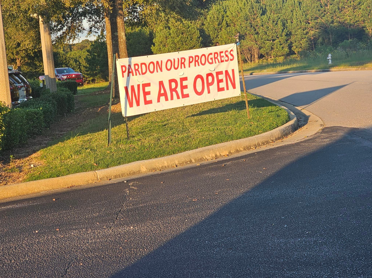 A sign that says pardon our progress we are open