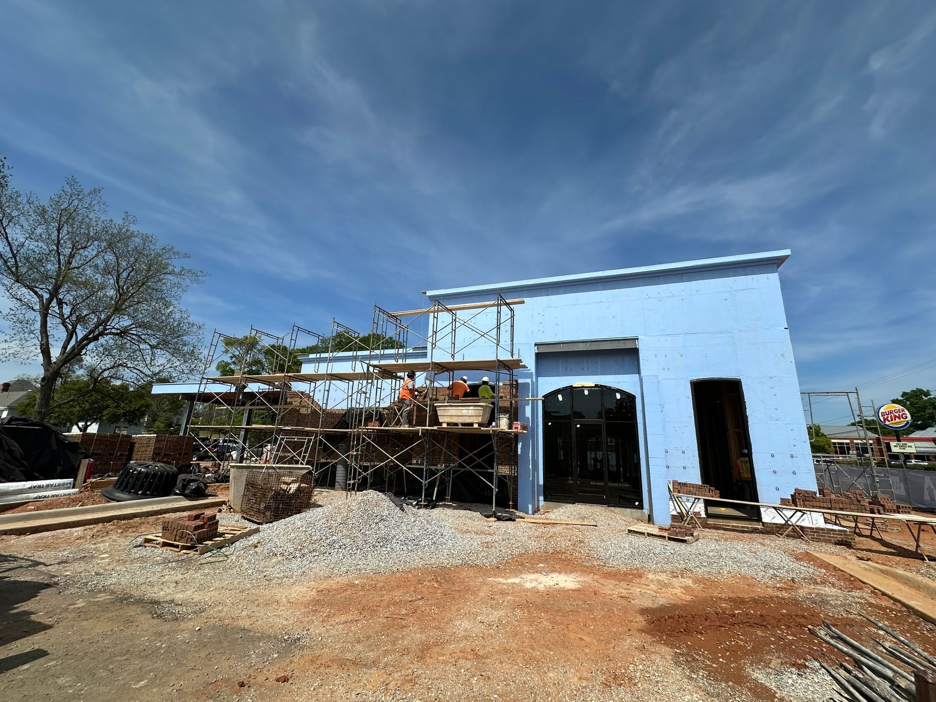 A light blue, single-story commercial building under construction with metal scaffolding and a gravel lot in front.