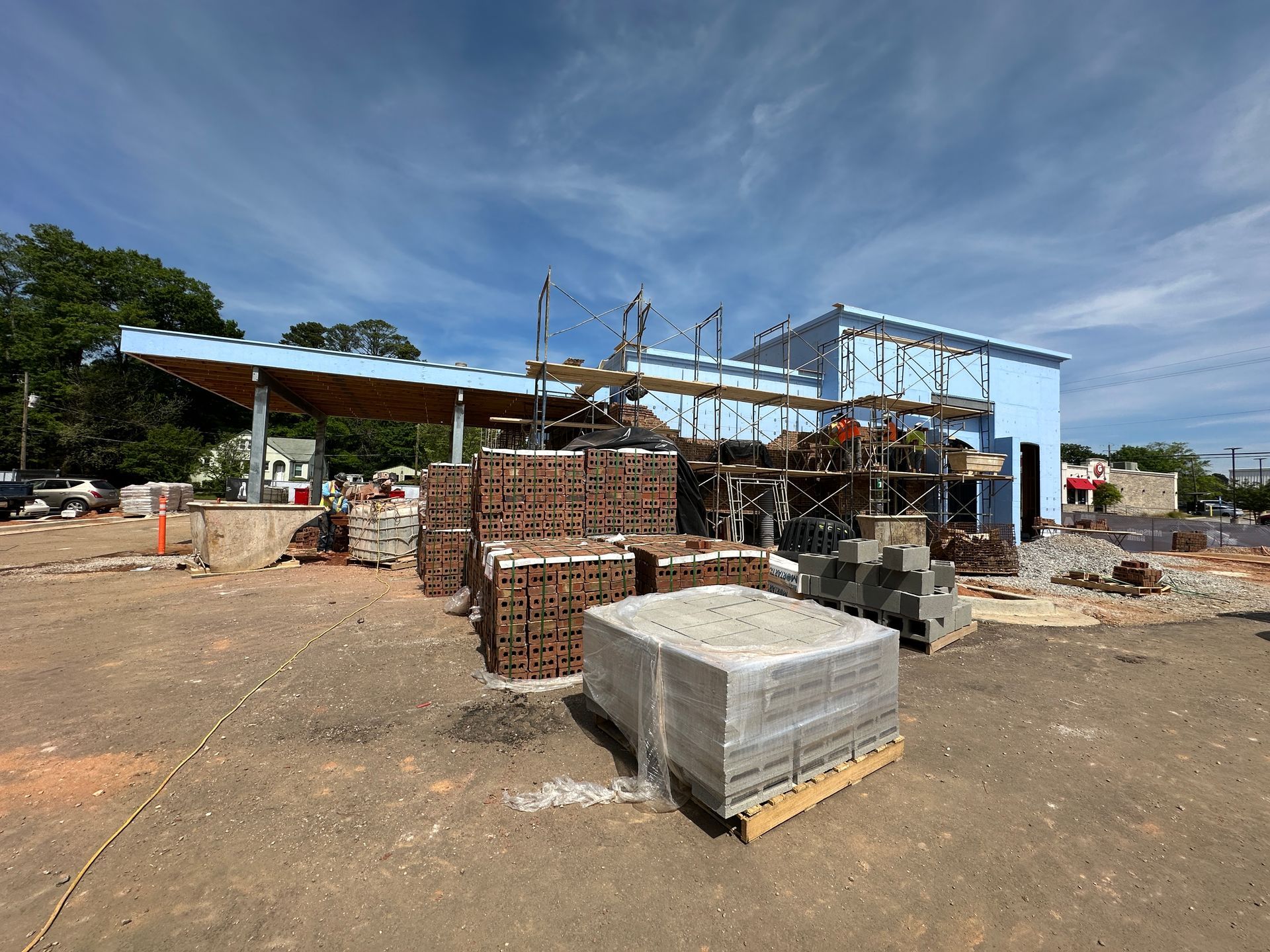 A construction site with stacked bricks and concrete blocks in front of a partially built light-blue building.