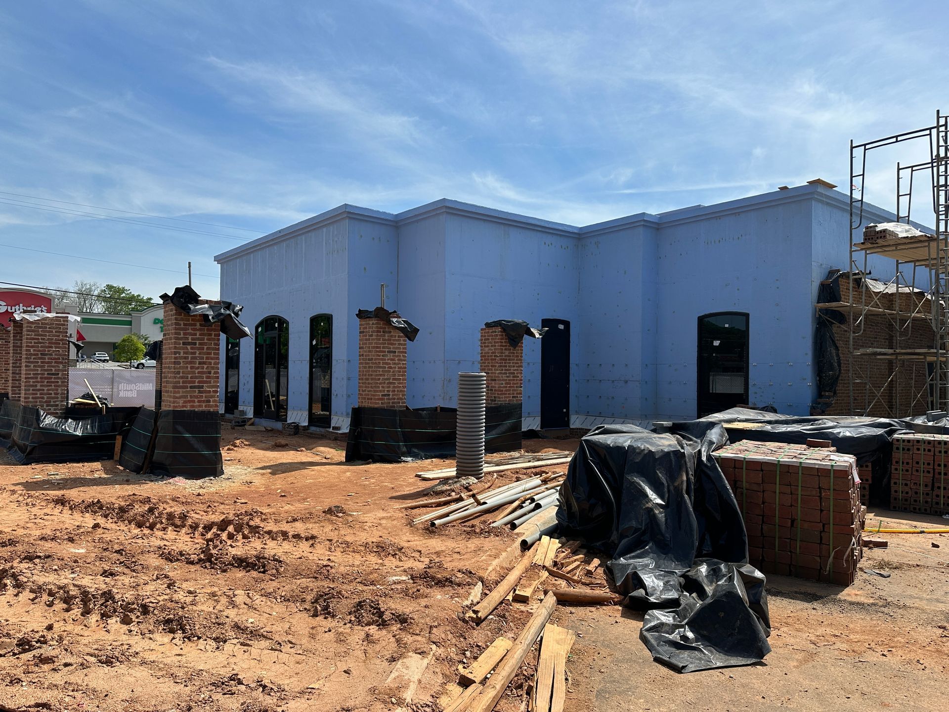 A light blue building under construction with exposed brick columns, a dirt ground, and stacks of brick materials.