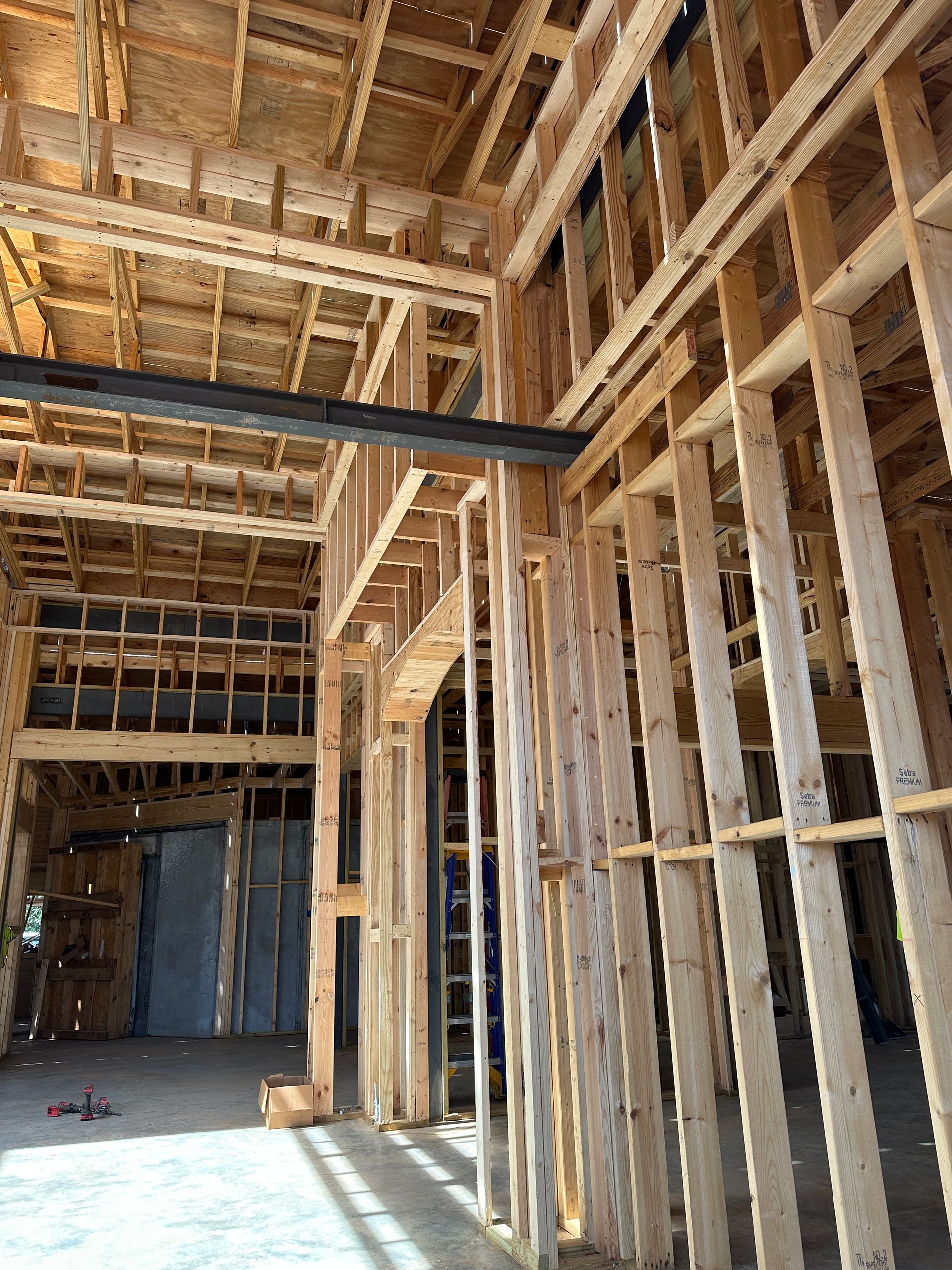 Interior view of a residential construction site featuring wooden wall framing and a large steel support beam.