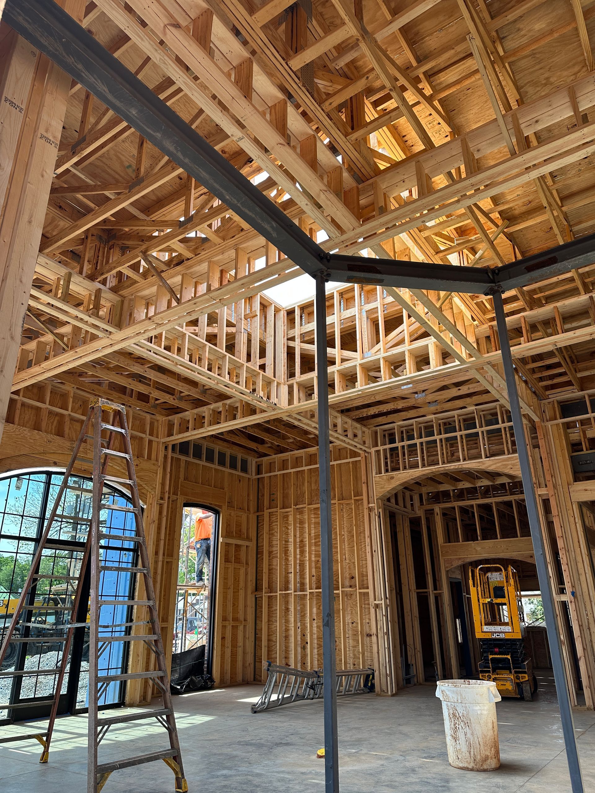 The interior of a house under construction with exposed wooden framing, a steel structural beam, and a step ladder.