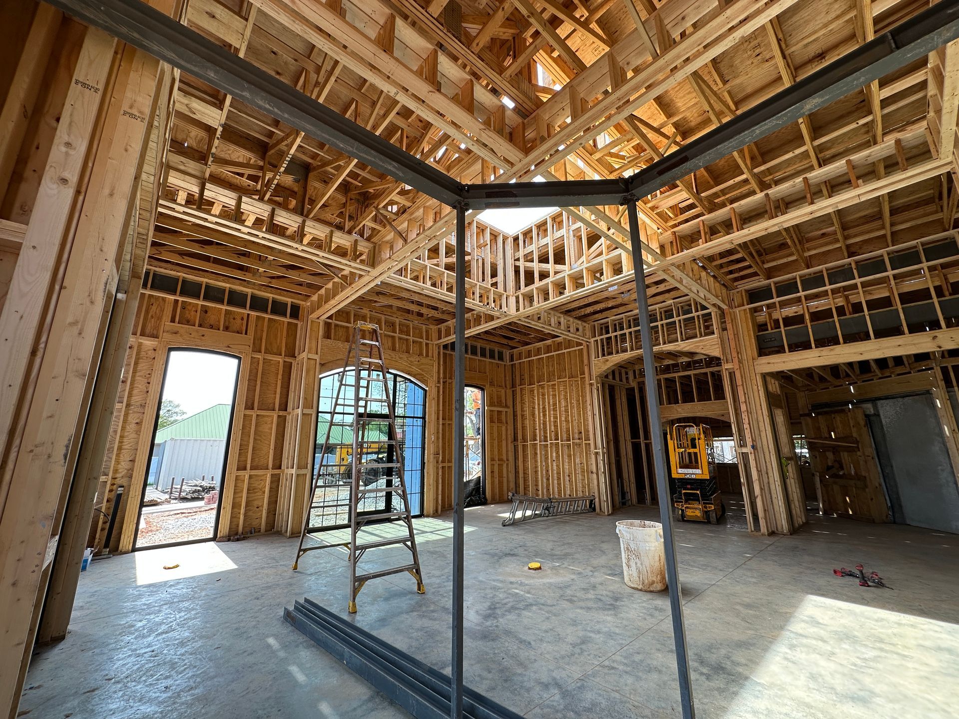 An interior view of a building under construction featuring exposed wooden framing, a metal pillar, and a step ladder.