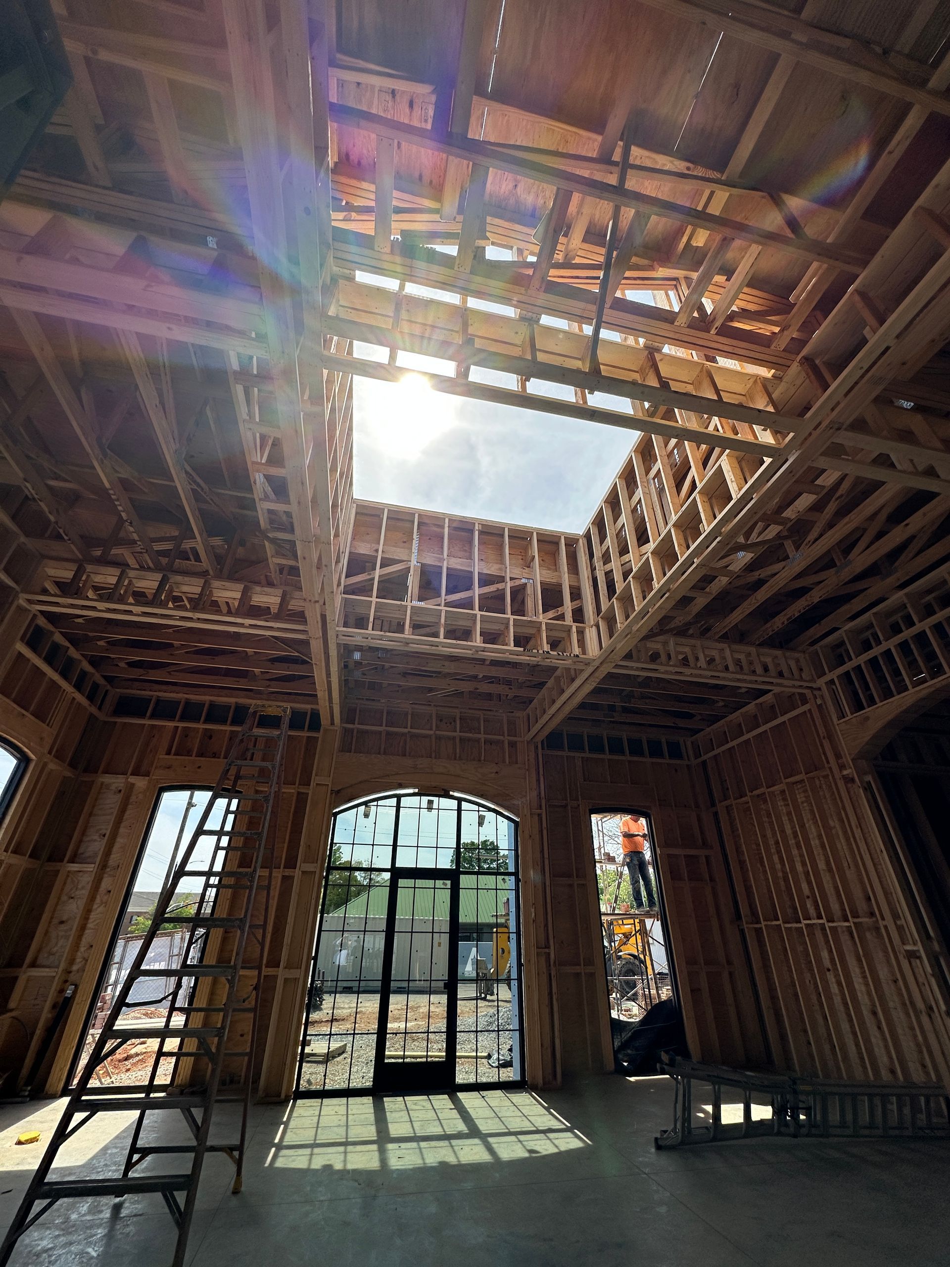 An interior view of a building under construction, featuring wooden framing, high ceilings, and a large central skylight.