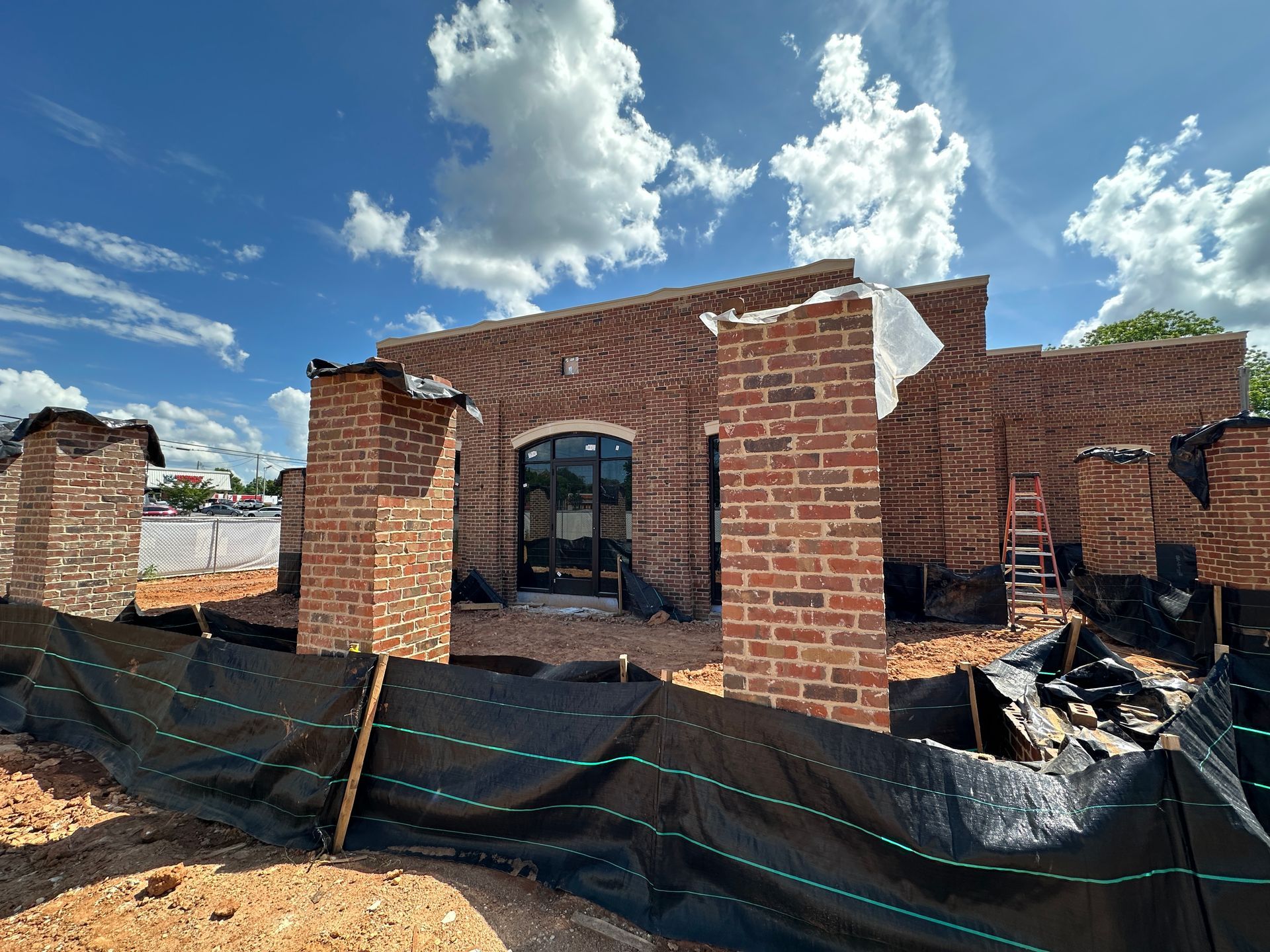 Partially built red brick bank under a blue sky, with black tarp and construction items in front.