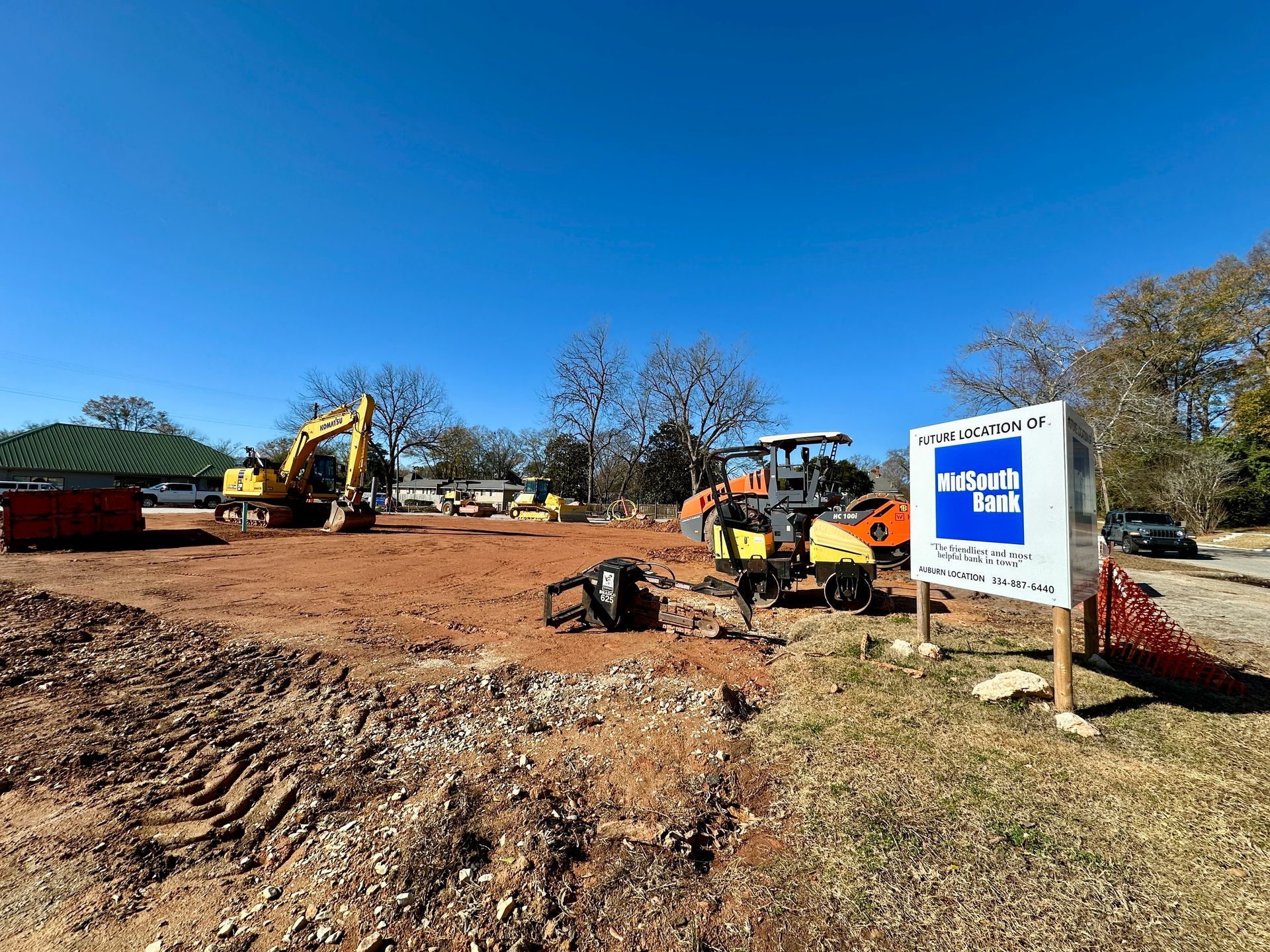 Construction site with heavy machinery, orange dirt, and a blue sky.