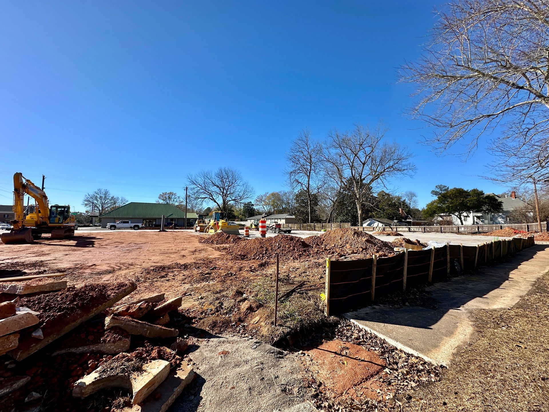 Construction site with excavator and bare trees under a clear blue sky.