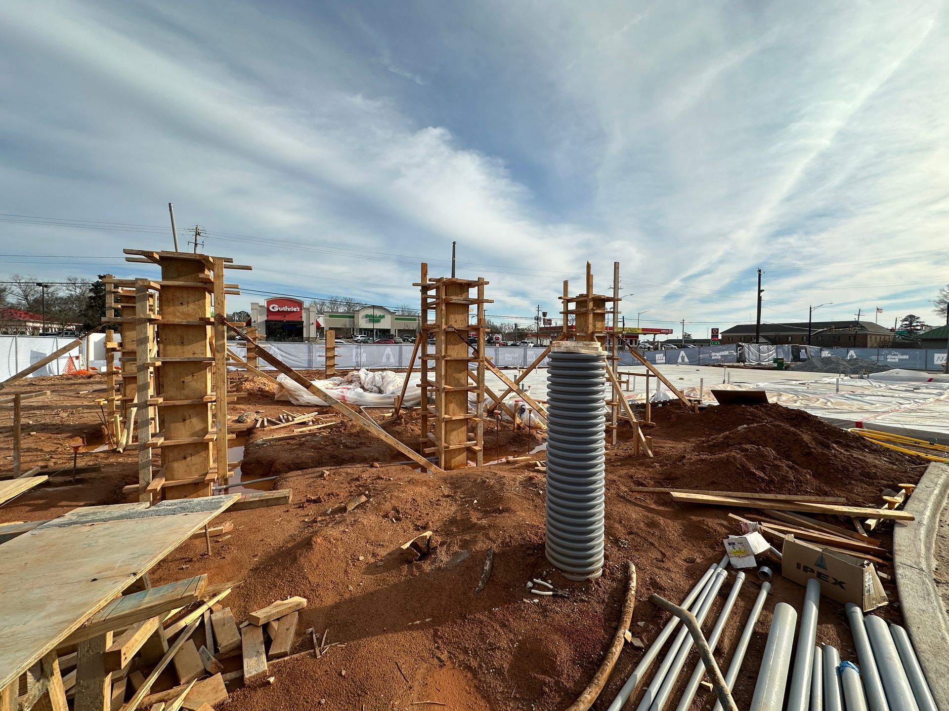 Construction site with wooden forms for columns and a corrugated pipe in the center. Bright sky, red dirt.