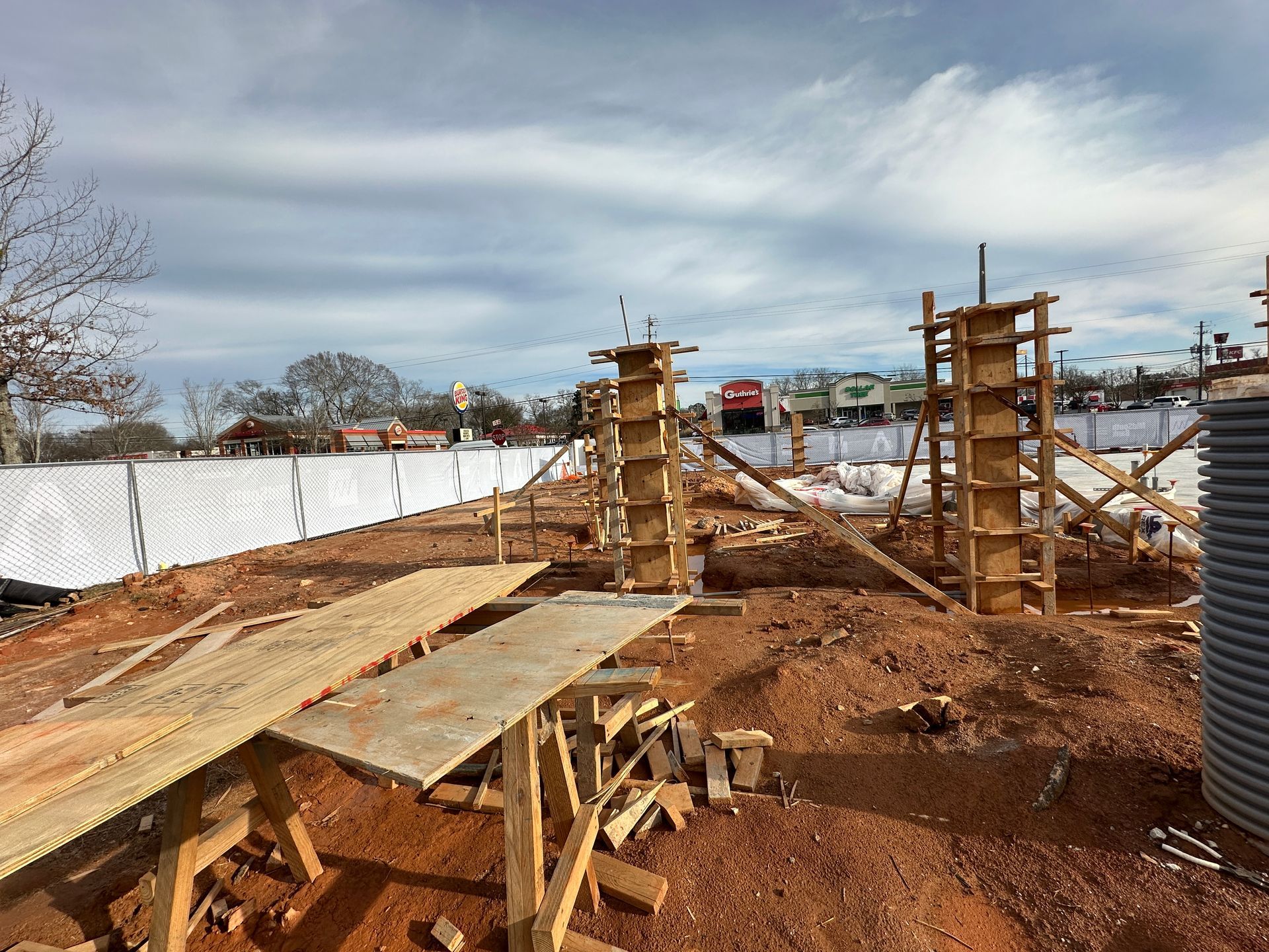 Construction site with wooden forms for pillars, red soil, and a cloudy sky.
