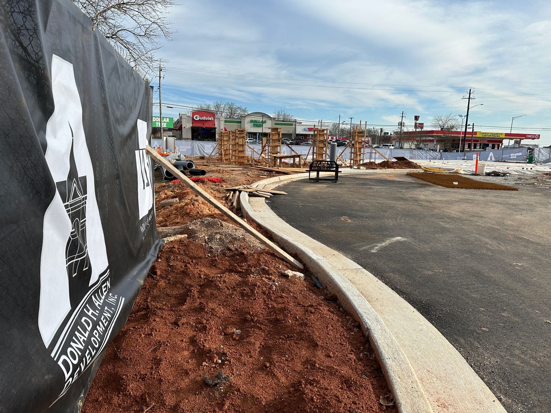 Construction site with a black and white banner. A curved curb, dirt, and a gas station are visible.