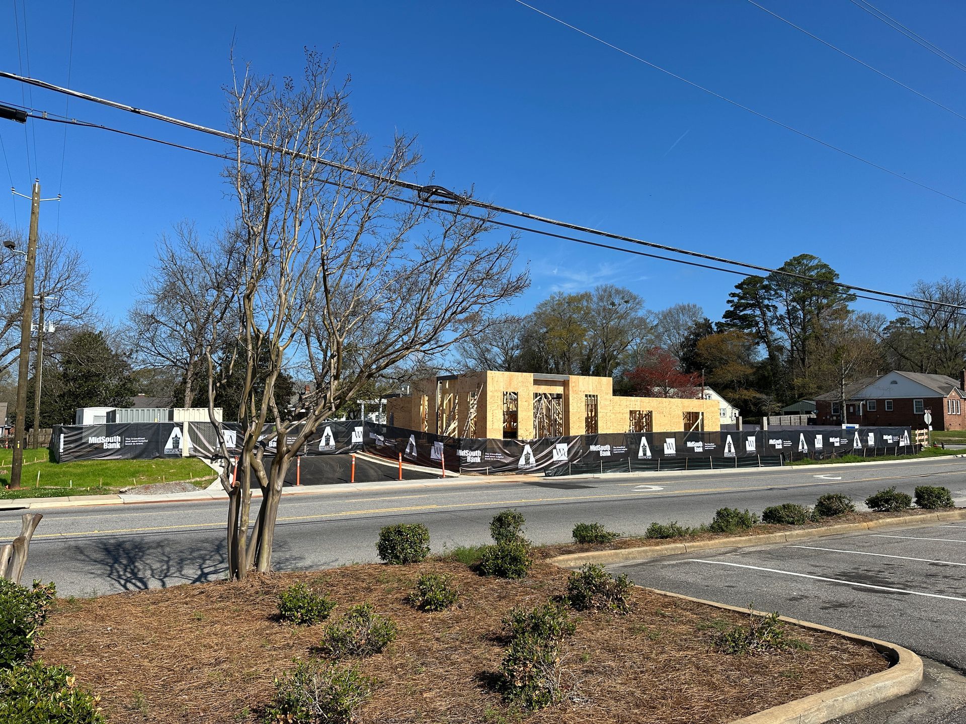 A wooden building frame under construction behind a black construction fence on a sunny day.
