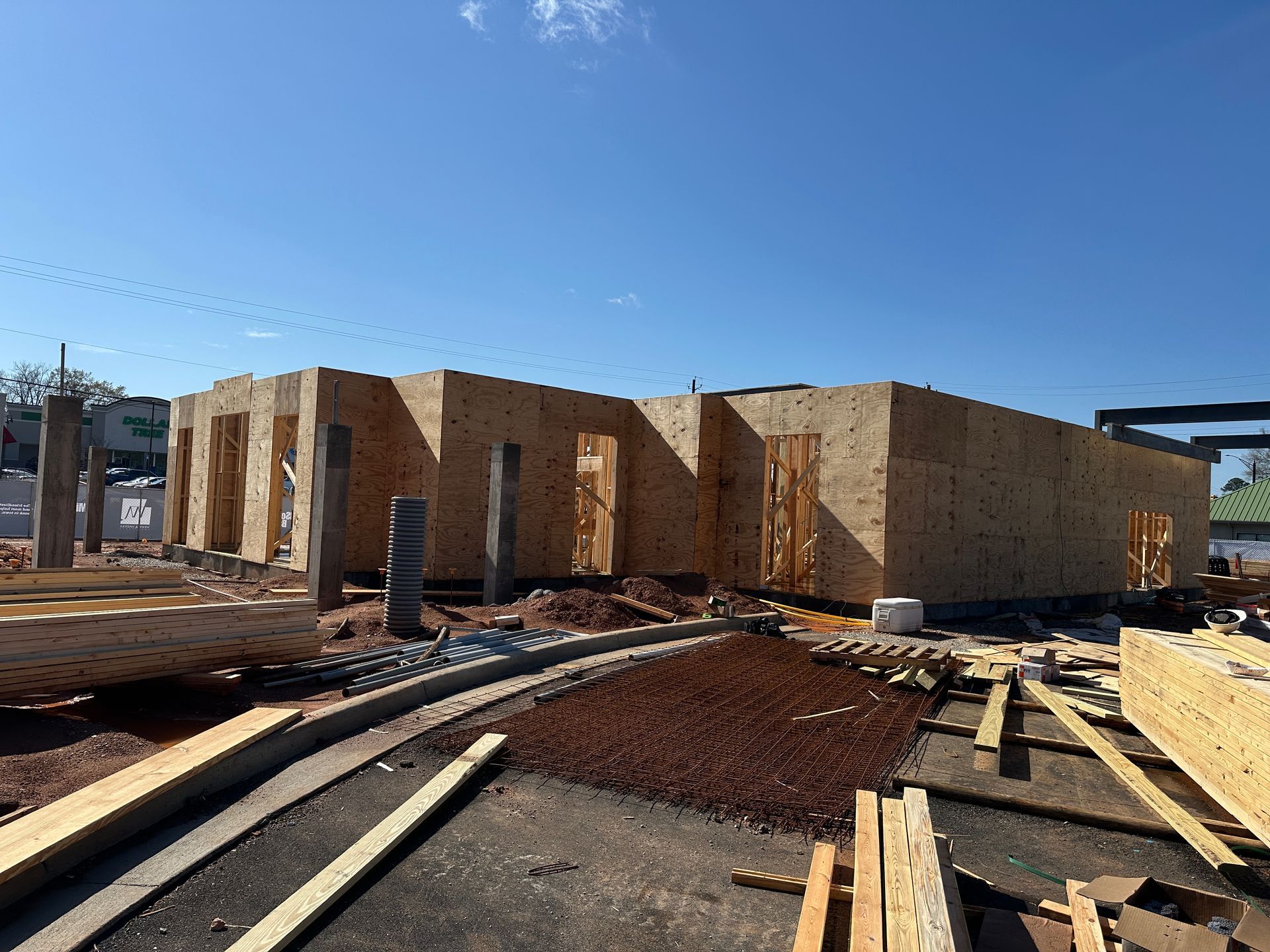 A construction site showing the wooden frame and plywood walls of a building under a clear blue sky.