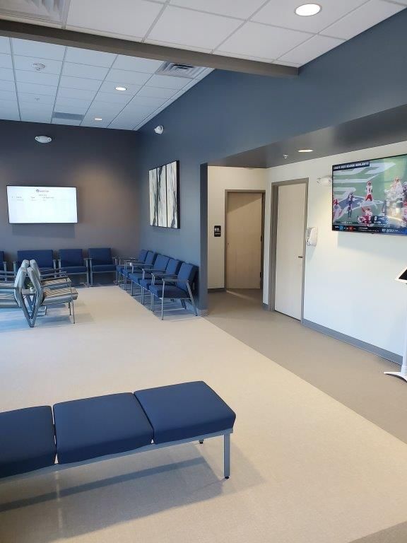 A waiting room with blue chairs and a flat screen tv