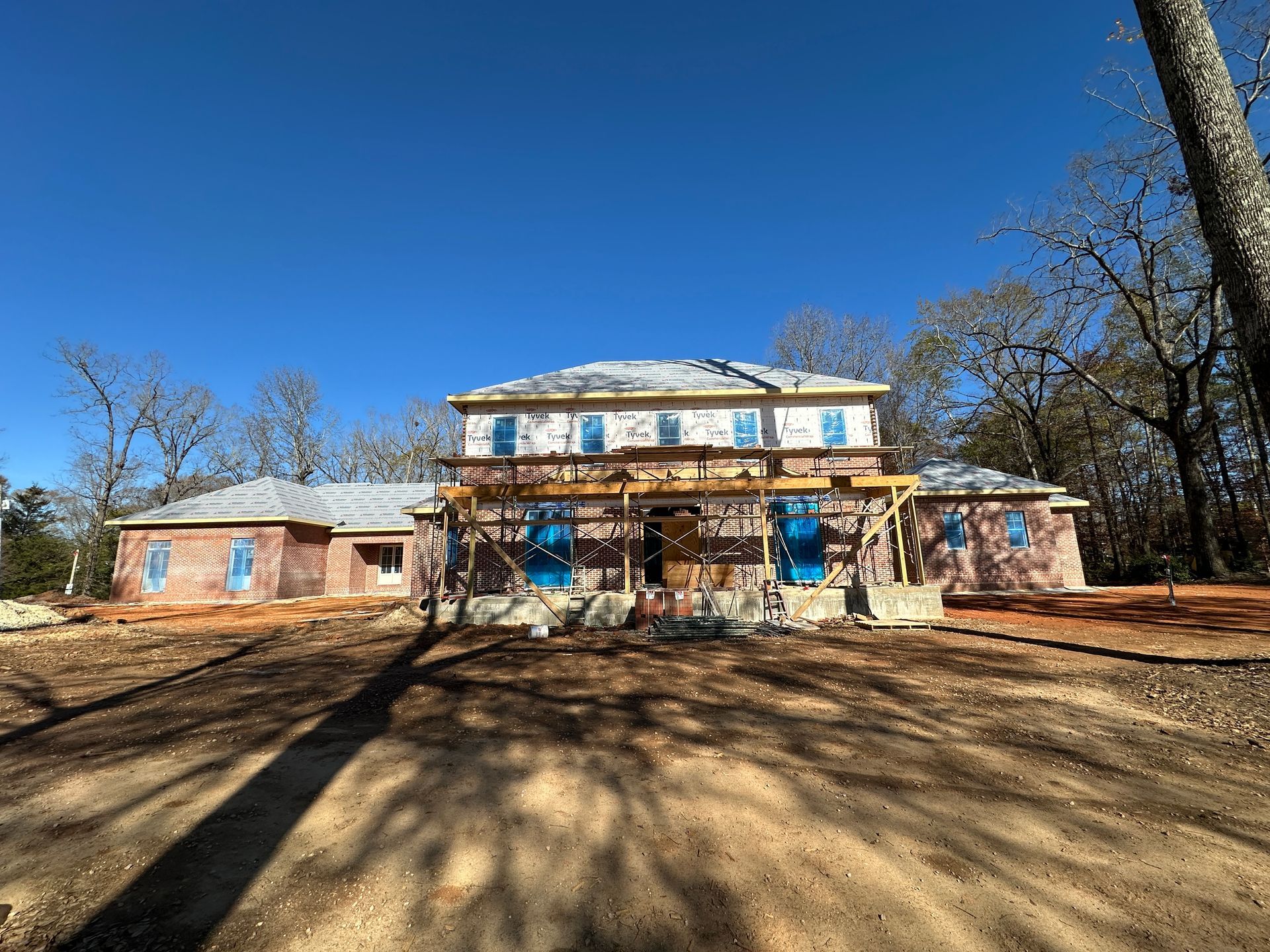 Two-story house under construction with exposed brick and blue protective coverings on windows.