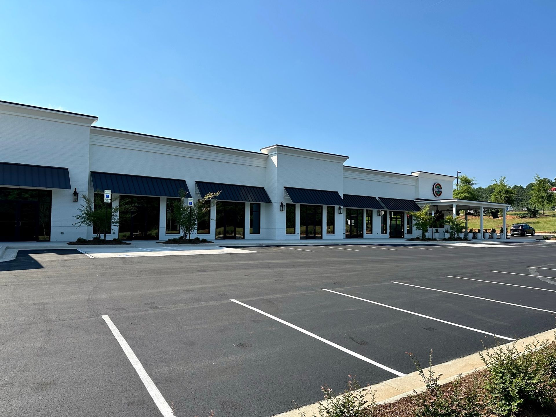 A large white building with black awnings and a parking lot in front of it.