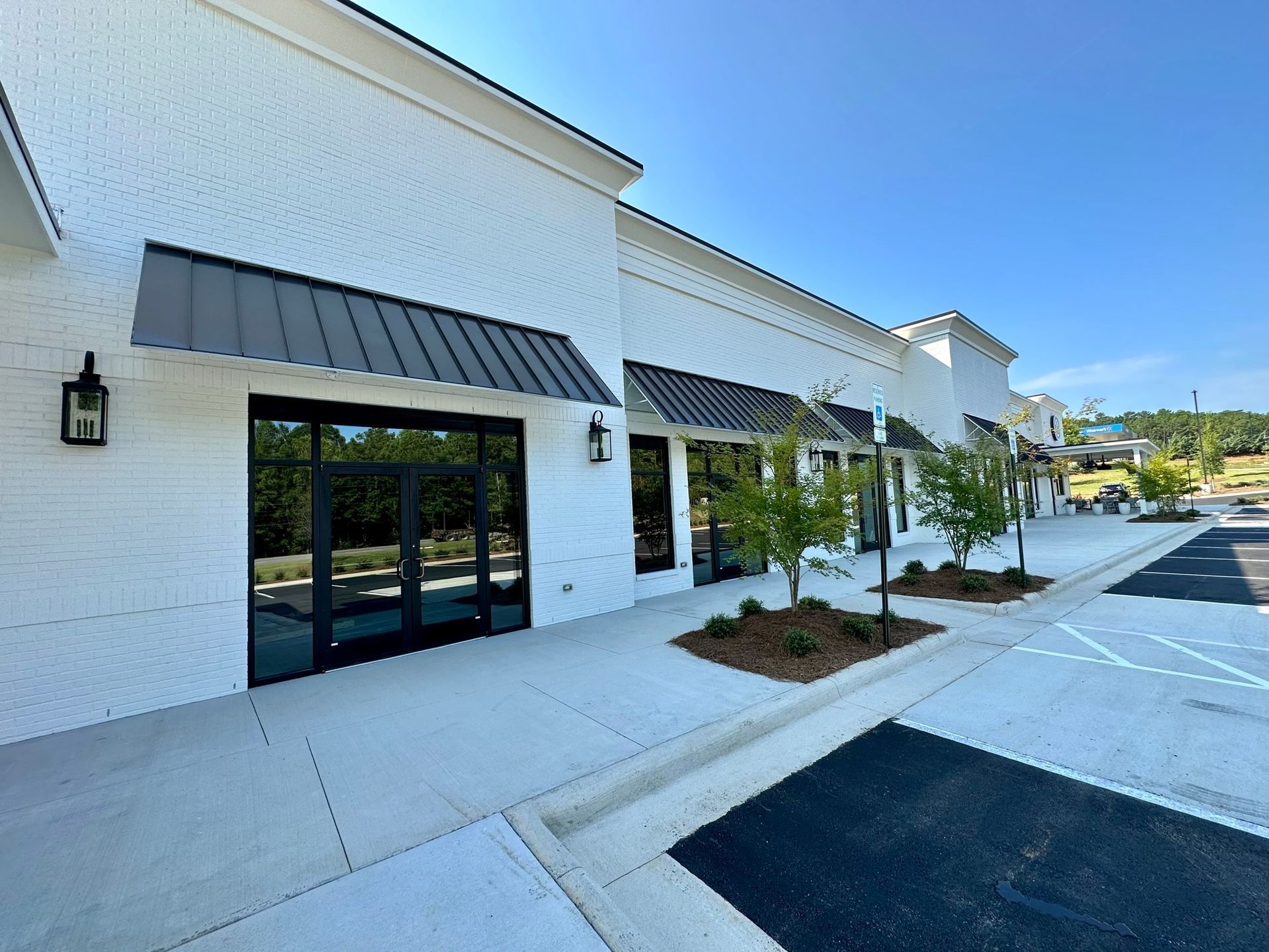 A white building with black awnings and a parking lot in front of it.