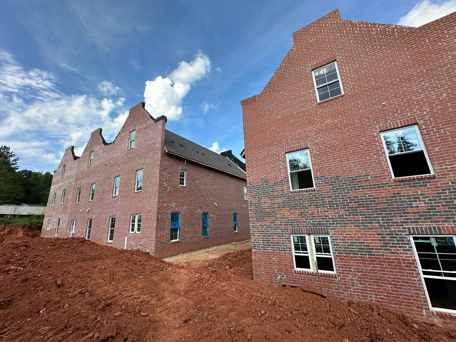Two brick buildings are being built next to each other in a dirt field.