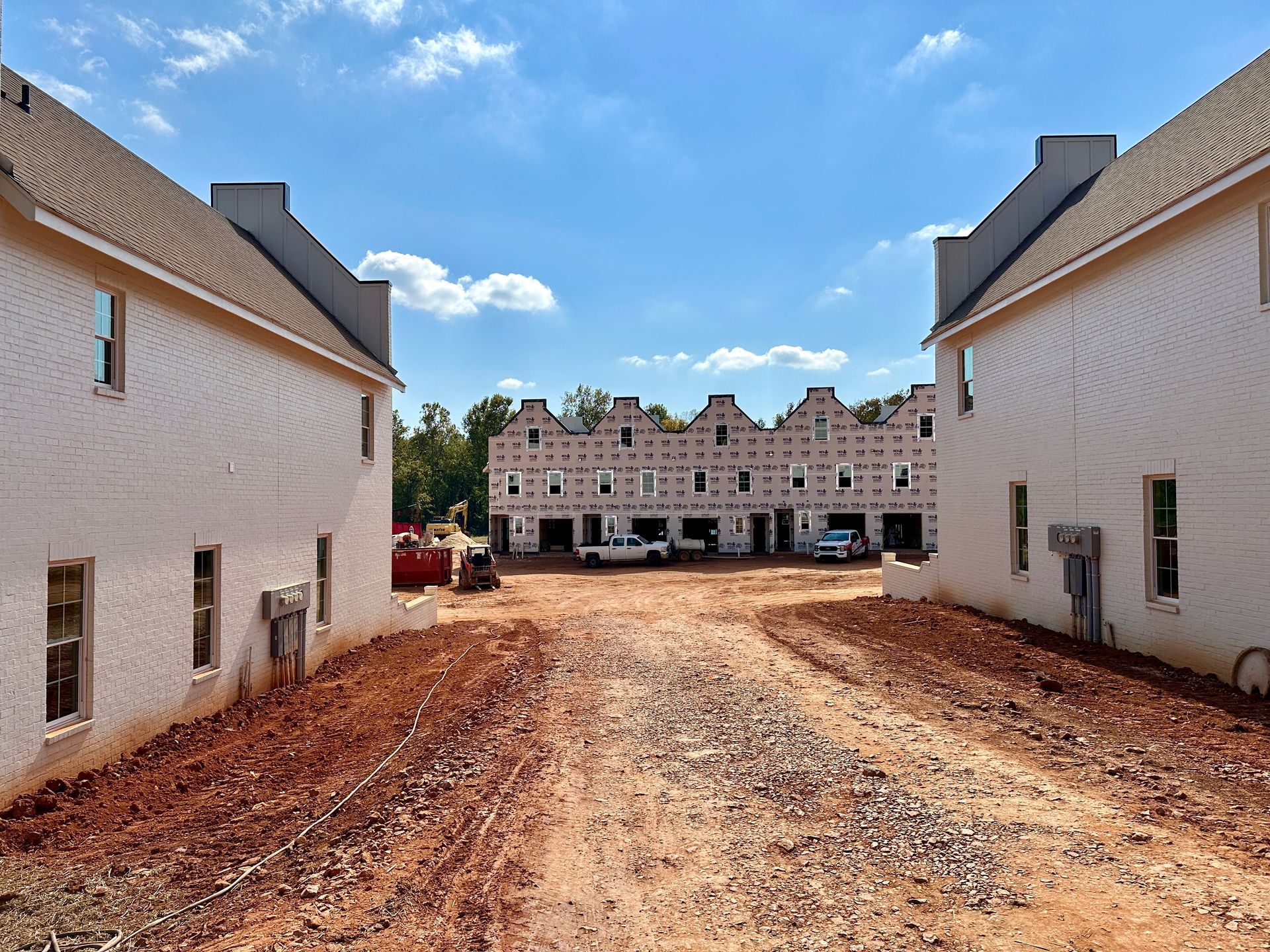 A row of white houses are being built on a dirt road