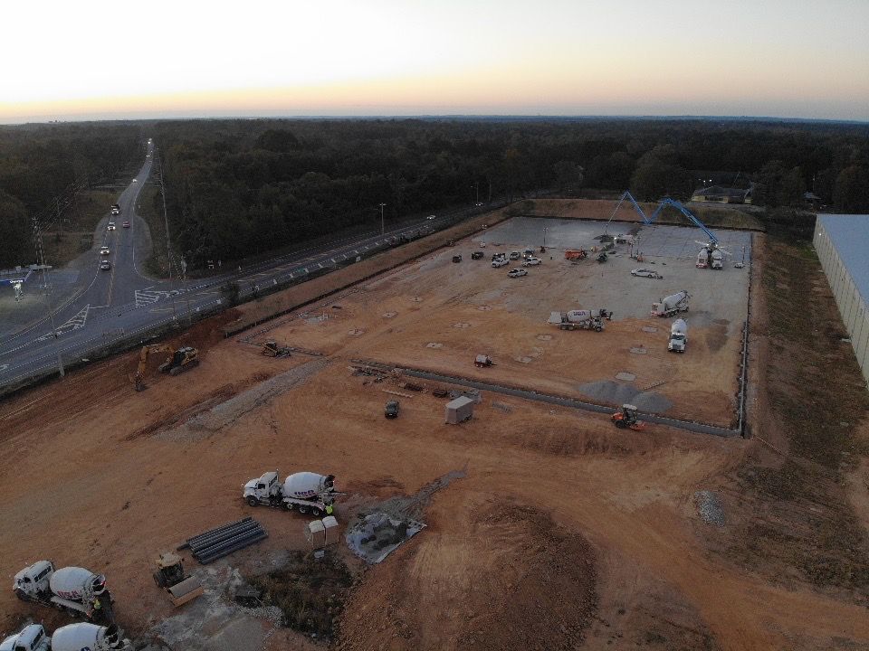 An aerial view of a construction site with trucks and a highway in the background.