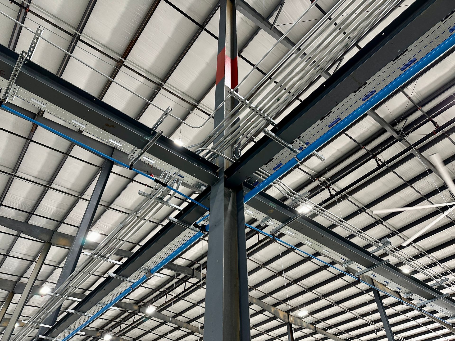 A large warehouse with a lot of pipes and wires hanging from the ceiling.