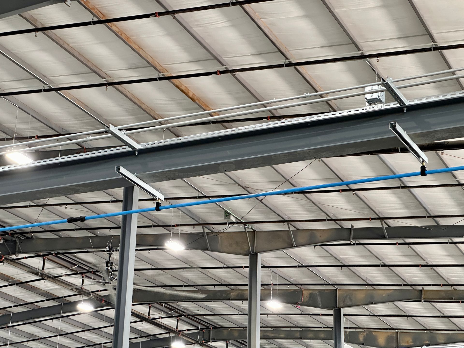 The ceiling of a large warehouse with a lot of pipes hanging from it.